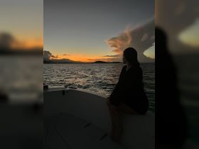 A serene sunset view with a silhouette of a woman sitting on the bow of a boat, creating a perfect backdrop for romantic evening cruises.