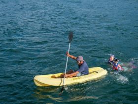 A man kayaks while a child swims nearby, showcasing a fun day of water activities. Perfect for family adventures and exploring the ocean.