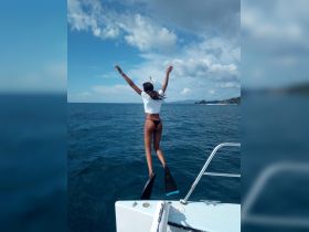 A joyful moment captured as a woman leaps off the boat into the ocean, embodying the thrill of water activities and adventure on a sunny day.
