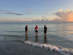 A group of three individuals wade into the gentle waves at sunset, enjoying a serene beach experience — perfect for family outings or beach adventures.