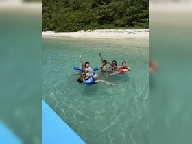 A lively group enjoys a refreshing swim in crystal-clear waters, celebrating together in a picturesque beach setting.