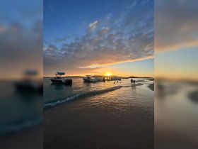 A picturesque sunset scene with boats anchored near the beach, where a group enjoys the water, creating a perfect backdrop for memorable summer evenings.