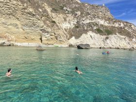 A serene scene of people swimming and kayaking in crystal-clear waters, surrounded by stunning cliffs — a perfect spot for a day of adventure and relaxation.