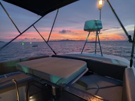 A serene sunset view from the deck of a boat, showcasing the tranquil waters and distant boats — perfect for evening cruises.