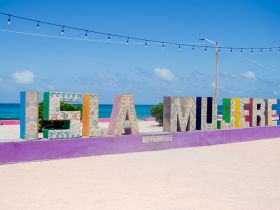 Colorful sign spelling 'ISLA MUJERES' against a backdrop of the ocean, capturing the vibrant essence of this popular destination.