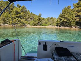 A serene view from a boat showcasing clear turquoise waters and a picturesque coastline, with people enjoying the beach — perfect for a relaxing day on the water.