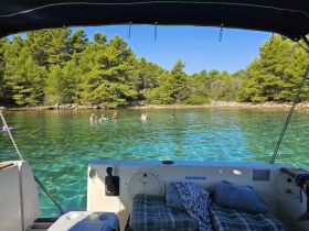 A lively group enjoys swimming in the crystal-clear waters of a secluded cove, with lush greenery in the background — a perfect spot for a refreshing summer getaway.