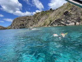 Two snorkelers explore the vibrant underwater world in crystal-clear waters, surrounded by stunning coastal scenery — a perfect adventure for marine enthusiasts.