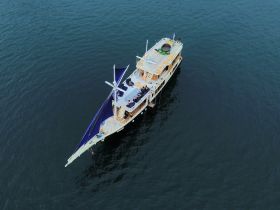 Aerial view of a beautifully designed boat underway, showcasing its spacious deck and vibrant sails, perfect for group adventures on the water.