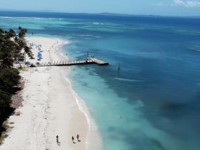 A picturesque beach scene featuring a pier and people enjoying the sun and water, perfect for a day of relaxation and fun in the tropics.