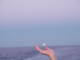 A serene moment captured as a hand reaches out towards the setting sun over the ocean, embodying the tranquility of a sunset cruise.