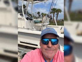 A man poses in front of the helm of a fishing boat, showcasing the console and fishing gear — perfect for a day out on the water.
