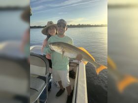 A happy couple proudly displays their catch while fishing at sunset, capturing the joy of a memorable day on the water.
