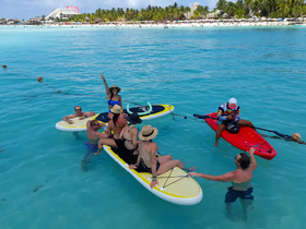 A lively group enjoys paddleboarding and swimming in crystal-clear waters, creating unforgettable memories at the beach.