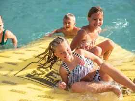 A joyful group of children enjoys a sunny day on a floating mat in clear waters, capturing the essence of summer fun and aquatic adventures.