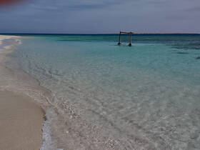 A stunning view of a serene beach with crystal-clear turquoise waters and soft sand, perfect for a relaxing getaway or a picturesque day by the sea.
