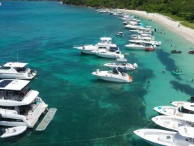 A vibrant scene at a sandbar with numerous boats anchored, where people enjoy swimming and relaxing in the clear turquoise waters — a perfect summer getaway.
