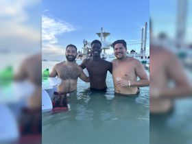 Three friends enjoy a fun day in the water, celebrating and swimming together, with a boat visible in the background — perfect for memorable summer outings.