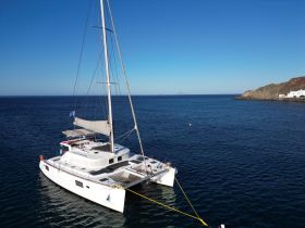 A stunning aerial view of a catamaran docked in serene waters, showcasing its sleek design against a backdrop of clear blue skies and rocky coastline.