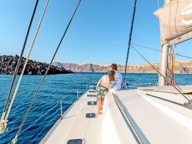 A couple enjoys a romantic moment on the deck of a sailboat, overlooking stunning coastal scenery — perfect for sunset cruises and intimate getaways.