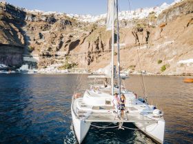 A couple enjoys a picturesque moment on a catamaran in Santorini, surrounded by stunning cliffs and vibrant scenery — perfect for island hopping adventures.