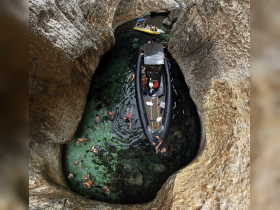 A thrilling scene of adventure as a group enjoys swimming in a stunning cave surrounded by crystal-clear waters, with boats anchored nearby for exploration.