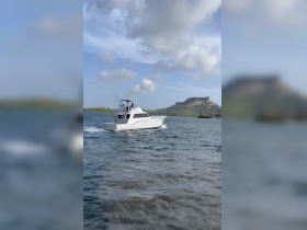 A sleek fishing boat navigates through the water, showcasing its design and speed against a scenic backdrop of hills and clouds.