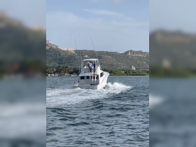 A sleek speedboat navigates through the water, showcasing its design and power against a scenic backdrop of hills and greenery.