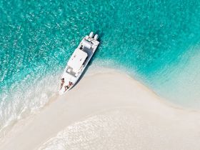 A stunning aerial view of a boat anchored near a sandy shore, showcasing the vibrant turquoise waters — perfect for a day of relaxation and adventure on the water.