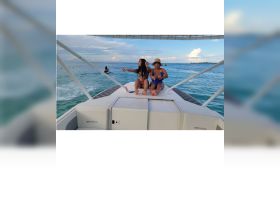 Two friends enjoy a fun moment on the bow of a boat, with a jet ski in the background, capturing the essence of a lively day on the water.