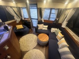 Cozy interior of a boat featuring a comfortable lounge area with plush seating and scenic views through large windows, perfect for relaxing while on the water.
