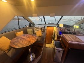 Interior view of a cozy boat cabin featuring a comfortable seating area and helm, perfect for relaxing while enjoying scenic waterfront views.
