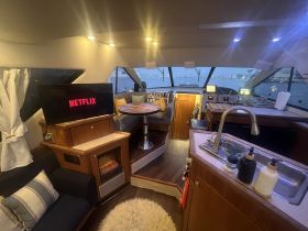 Interior view of a luxurious boat cabin featuring a cozy seating area, a helm, and a TV displaying Netflix, perfect for relaxing on the water.