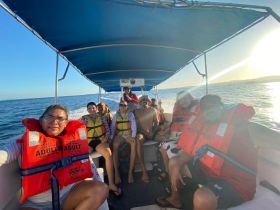 A cheerful group enjoys a boat ride at sunset, wearing life jackets and capturing memorable moments on the water.