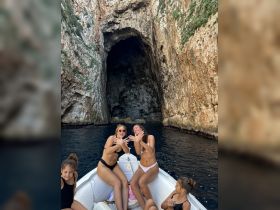 A joyful group of friends poses on a small boat near a stunning cave, capturing a fun moment during their aquatic adventure.