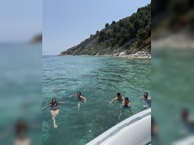 A lively group enjoys a refreshing swim in crystal-clear waters, surrounded by stunning coastal scenery — perfect for summer adventures and beach outings.