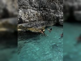 A group of friends enjoys swimming in crystal-clear waters near stunning rock formations, capturing the essence of a perfect day on the water.