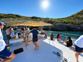 A lively group enjoys a sunny day aboard a boat, relaxing and taking in the beautiful coastline — perfect for a fun day on the water.