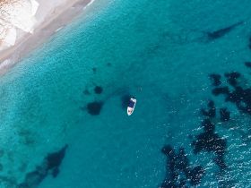 An aerial view captures a boat anchored in crystal-clear waters, with a person swimming nearby — a perfect scene for water adventures and relaxation.