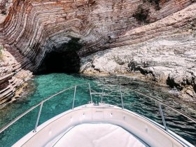 A stunning view from the bow of a boat approaching a natural cave, surrounded by vibrant turquoise waters and layered rock formations — a perfect spot for exploration and adventure.
