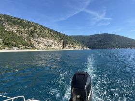 A scenic view from a boat cruising along a beautiful coastline, showcasing the lush green hills and clear blue waters — perfect for exploring hidden beaches and enjoying nature.