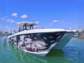 A striking speedboat featuring a detailed fish mural on its side, captured in clear waters with a sunny sky — perfect for fishing enthusiasts and water adventures.