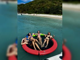 A fun group of friends relaxes on a floating mat in crystal-clear waters, enjoying a perfect day of sun and laughter at the beach.