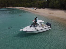 A group enjoys a sunny day at the beach with a boat anchored nearby, perfect for swimming and relaxation in the clear waters.