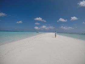 A person stands on a stunning white sand beach, capturing the breathtaking scenery of turquoise waters and a distant boat — a perfect moment for beach lovers and photographers.