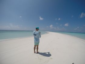 A traveler stands on a pristine white sand beach, capturing the stunning scenery of turquoise waters and a clear blue sky — a perfect moment on a tropical getaway.