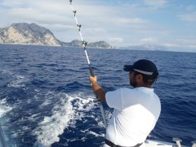 A man enjoys fishing on a boat with stunning coastal scenery in the background, capturing the essence of a perfect day on the water.