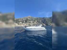 A sleek yacht glides through the clear blue waters, set against a stunning coastal backdrop of cliffs and colorful buildings, perfect for exploring scenic destinations.