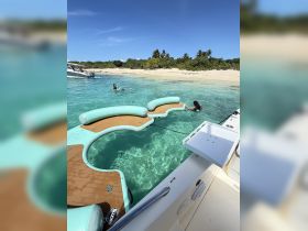 Guests enjoy a sunny day swimming near a floating mat in crystal-clear waters, with a picturesque beach backdrop — perfect for summer fun and relaxation.