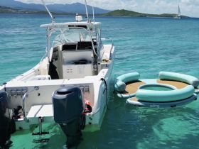 A motorboat anchored in clear turquoise waters, featuring a floating mat nearby, perfect for relaxation and fun on the water.